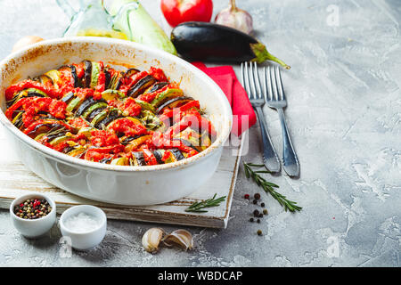 Ratatouille végétarien de aubergines, courgettes, tomates et sauce tomate et poivrons aux herbes en forme de céramique avant la cuisson. Style rustique. Banque D'Images