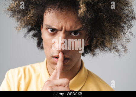 Gros plan Photo de angry caucasian man with afro hairstyle froncer et doigt de maintien à sa bouche sur fond gris isolé Banque D'Images