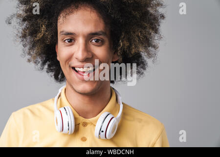 Photo de cheerful man avec coiffure afro portant des écouteurs smiling at camera isolated over grey background Banque D'Images