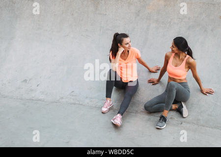 Image femmes fitness sportswear en sourire et parler ensemble tout en étant assis sur des terrain de sport Banque D'Images