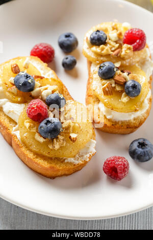 Crostini avec ricotta, Poires poêlées, noix et miel, décoré avec des framboises et bleuets Banque D'Images