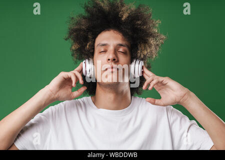 Gros plan Photo de jeune homme détendue avec les yeux fermés à l'écoute de la musique avec des écouteurs sur fond vert isolé Banque D'Images