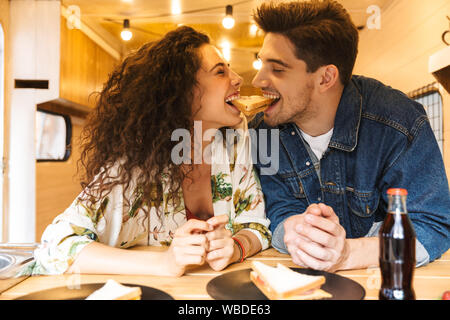 Portrait of happy couple homme et femme en riant tout en mangeant ensemble dans sandwich cuisine confortable à l'intérieur de la remorque Banque D'Images