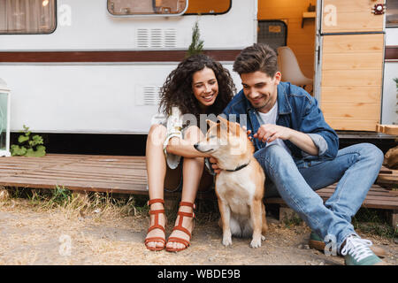 Portrait de beau couple homme et femme de flatter le chien rouge alors qu'il était assis près de maison sur roues à l'extérieur Banque D'Images