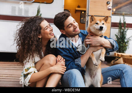 Cheerful young couple parler tout en se tenant à l'campvan, flatter un chien Banque D'Images