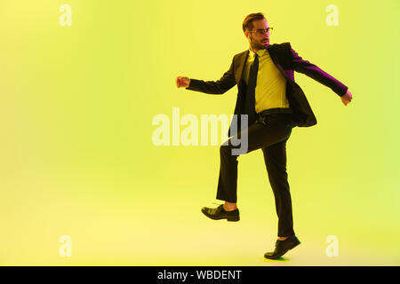 Handsome young businessman wearing costume formel isolé marche sur fond jaune, à l'aide d'écouteurs sans fil Banque D'Images