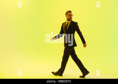 Handsome young businessman wearing costume formel isolé marche sur fond jaune, à l'aide d'écouteurs sans fil Banque D'Images