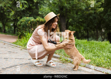 Portrait de nice woman wearing dress de caresser le chien et sourit tout en s'accroupissant dans parc d'été Banque D'Images