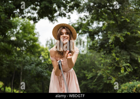 Portrait of cute caucasian woman wearing dress walking with dog and smiling in summer park Banque D'Images