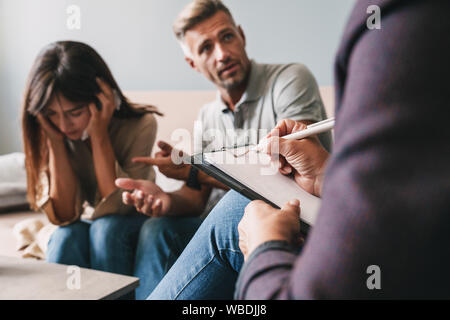 Photo de colère irrité couple homme et femme d'avoir une conversation avec un psychologue sur séance de thérapie dans la chambre Banque D'Images