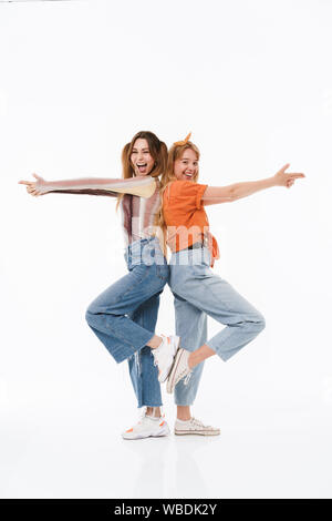 Photo de deux jeunes filles portant des vêtements colorés joyeux debout dos à dos et faisant des gestes d'armes à feu avec les doigts isolated over white background Banque D'Images