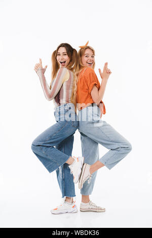 Photo de deux jeunes filles portant des vêtements colorés et de faire des gestes d'armes à feu avec les doigts isolated over white background Banque D'Images