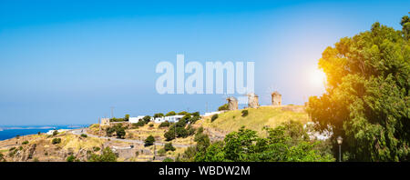 Paysage panoramique vue sur l'île de Patmos au coucher du soleil avec trois moulins à vent sur la colline contre fond de ciel bleu un jour d'été. Banque D'Images