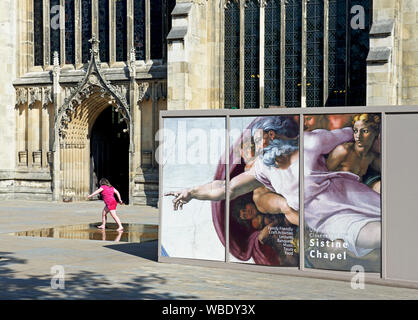 Fille jouant à côté affiche annonçant une exposition d'art de l'œuvre de Michel-Ange, à l'extérieur de la cathédrale, Hull, East Yorkshire, England UK Banque D'Images