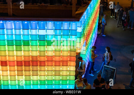 Stadtfest Brugg 24 août 2019. Photographie de rue. Bleu, vert, jaune et rouge en plastique lumineux mur de Kubus Kolor avec les gens sur le dessus. Banque D'Images