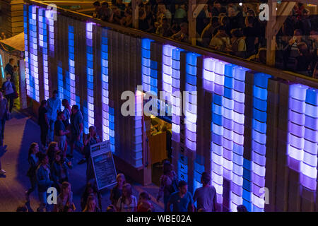 Stadtfest Brugg 24 août 2019. Photographie de rue. Lilas et bleu de mur en plastique éclairé Kubus Kolor avec les gens sur le dessus et les gens à pied Banque D'Images