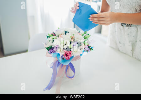 Femme ouvre enveloppe avec carte laissée dans bouquet de fleurs en boite cadeau sur la cuisine. Surprise. Présent pour les vacances. Livraison de fleurs Banque D'Images