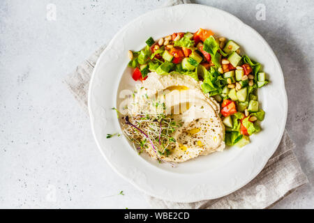 L'hoummos avec une salade de légumes et les graines germées dans une assiette blanche. Banque D'Images