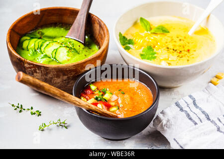 Trois différentes soupes crème de légumes dans des bols sur un fond gris. Le maïs, le concombre et le gazpacho de soupes. Banque D'Images