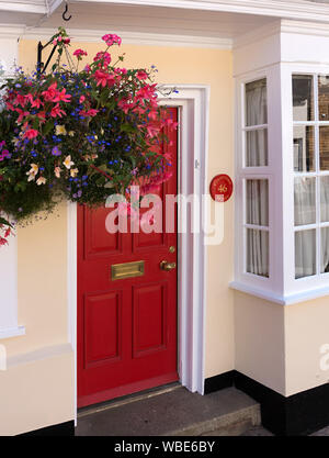 Fraîchement peint de couleur crème maison / chalet avec porte avant rouge, blanc guillotine et Hanging Basket, Uppingham, England, UK. Banque D'Images