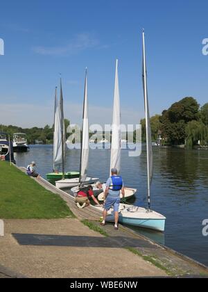 Quatre petits voiliers sont amarrés sur les rives de la Tamise avec un homme portant le Club de voile de Beaconsfield atteindre bib. Banque D'Images