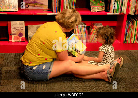 Lecture de la mère à son enfant sur l'floorin le coin d'un magasin de livres Banque D'Images