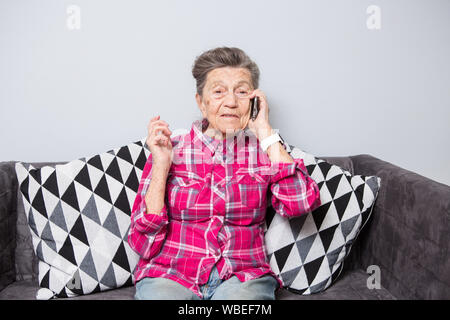 Vieux thème personne utilise la technologie. Happy mature joie sourire cheveux gris active Caucasian woman rides accueil dans le salon sur le canapé et à l'aide d'un Banque D'Images