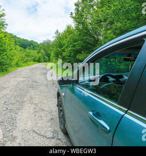 Vus sur l'ancienne route forestière. bleu cyan véhicule stationné sur le chemin d'asphalte fissuré en amont entre les arbres. vue depuis la porte du conducteur et rétroviseur latéral. perdu d Banque D'Images