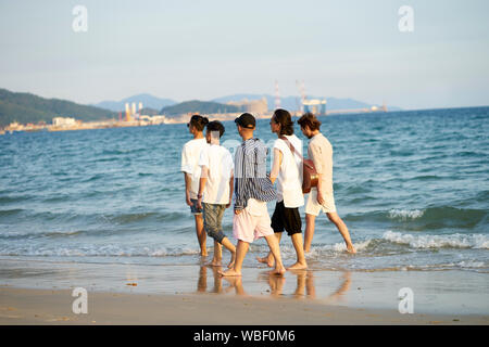 Groupe de cinq jeunes hommes asiatiques marcher dans l'eau de mer sur la plage Banque D'Images