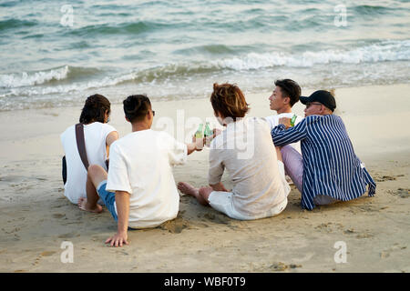Groupe de jeunes hommes adultes asiatiques bière potable bouteilles cliquant sur grillage plage, vue arrière Banque D'Images