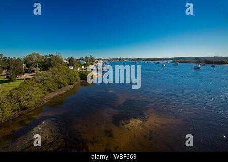 Vaste calme les eaux bleues de la rivière Myall avec les bateaux de plaisance et de la jetée et de la ville de jardins de thé parmi les arbres des berges sous ciel bleu, NSW Australie Banque D'Images