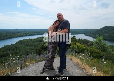 Couple aimant de 30 à 40 ans à l'extérieur et debout sur une colline avec une rivière qui coule à travers les bois l'arrière-plan Banque D'Images