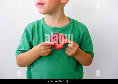 Petit garçon en t-shirt vert avec peach en forme de cœur dans ses mains Banque D'Images