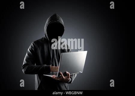 La cybercriminalité, le piratage et la criminalité technologique. aucun visage hacker avec ordinateur portable sur fond noir avec le chemin de détourage. Banque D'Images