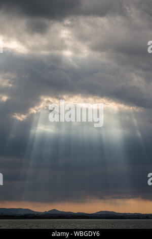 Du soleil au coucher du soleil, avec de sombres nuages en arrière-plan, un ciel orange, et du lac Trasimeno (Ombrie, Italie) ci-dessous Banque D'Images