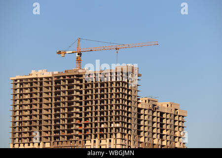 Grue de construction inachevée et tour d'habitation sur fond de ciel bleu clair Banque D'Images