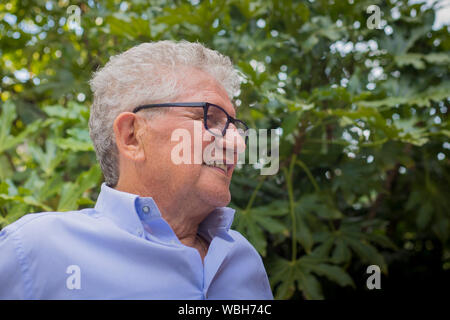 Portrait d'un vieil homme blanc gris avec des cheveux bouclés et des lunettes, à l'écart avec expression souriante. Banque D'Images