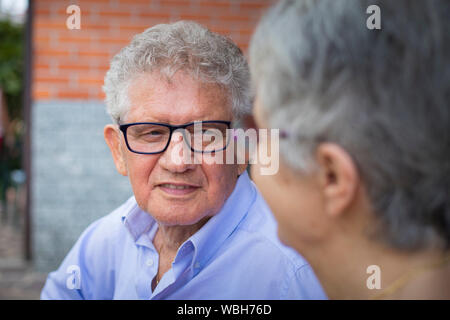 Portrait d'un homme plus âgé avec des cheveux gris et des lunettes, souriant à sa femme dans un paysage en plein air. La femme n'est pas nette. Banque D'Images