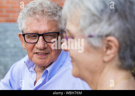 Portrait d'un homme plus âgé avec des cheveux gris et des lunettes, souriant à sa femme dans un paysage en plein air. La femme n'est pas nette. Banque D'Images
