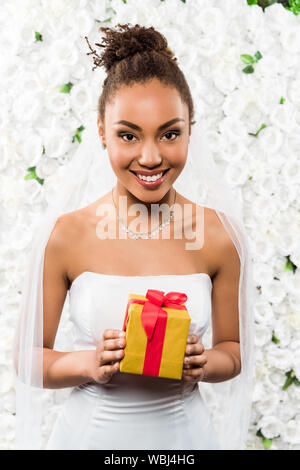 Cheerful african american promise au voile holding présents près des fleurs Banque D'Images