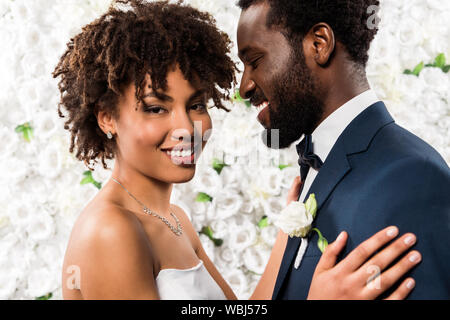 Cheerful african american bride hugging beau époux près de fleurs Banque D'Images