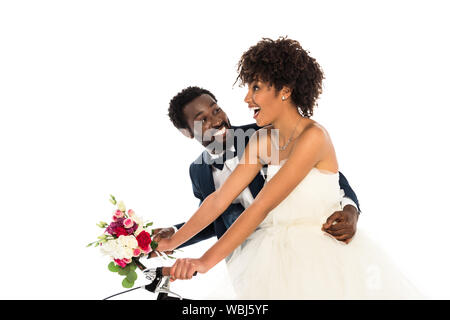 Happy african american époux près de cheerful bride avec fleurs riding bicycle isolated on white Banque D'Images