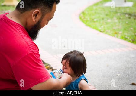 Homme barbu à l'eau donne un tout-petit enfant. La famille asiatique, la paternité et parental concept. Banque D'Images