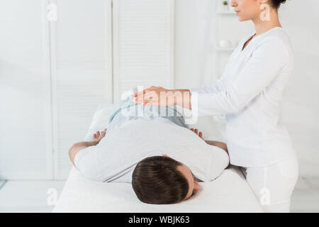 Portrait de guérisseur mettant les mains au-dessus du dos de l'homme sur la table de massage Banque D'Images