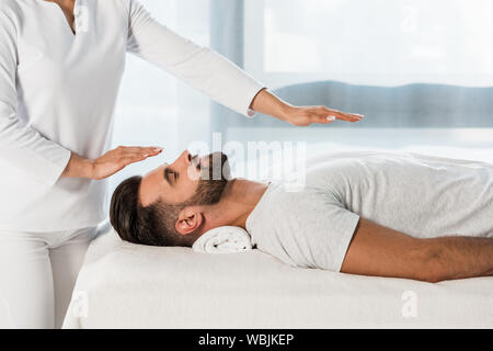 Portrait de guérisseur mettant les mains au-dessus de corps d'homme barbu Banque D'Images