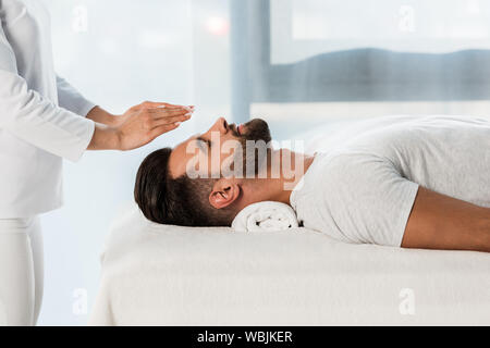 Portrait de guérisseur mettant les mains au-dessus de la tête d'homme barbu aux yeux clos Banque D'Images