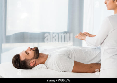 Portrait de guérisseur mettant les mains au-dessus du corps de l'homme barbu aux yeux clos Banque D'Images