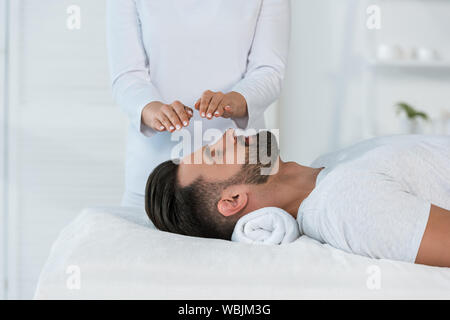 Portrait de guérisseur mettant les mains au-dessus de la tête de bel homme sur la table de massage Banque D'Images