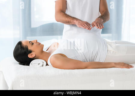 Portrait de guérisseur mettant les mains au-dessus du ventre de femme enceinte brune Banque D'Images