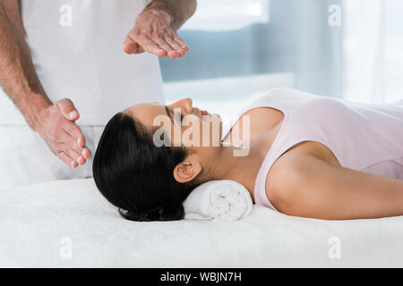 Portrait de guérisseur mettant les mains au-dessus de la tête de fille brune sur la table de massage Banque D'Images